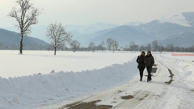 在寒冷的冬日，一对夫妇沿着积雪的道路散步视频素材