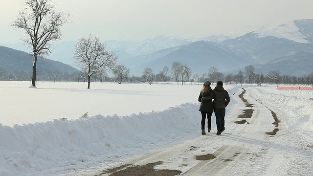 在寒冷的冬日，一对夫妇沿着积雪的道路散步视频素材