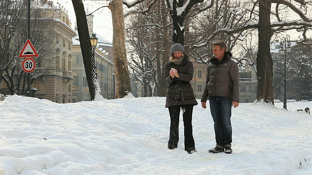 在冬日，一对夫妇走过白雪公园，女人扔雪视频素材