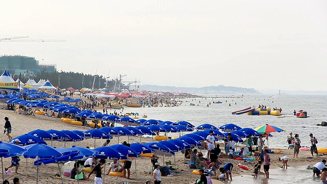 韩国江原道江陵的京浦台海滩上，人们在帐篷和遮阳板上放松视频素材