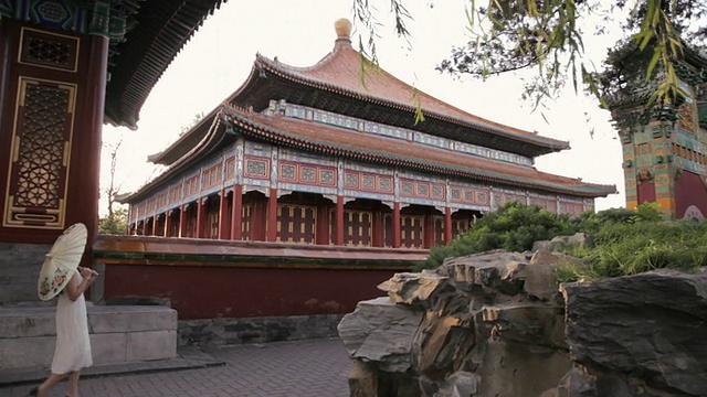 中国北京，一名年轻女子撑着雨伞走过中国寺庙的庭院视频素材