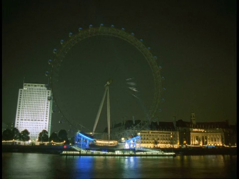 T/L蓝色的伦敦眼在夜空中转动，泰晤士河在前景，市政厅在背景视频素材