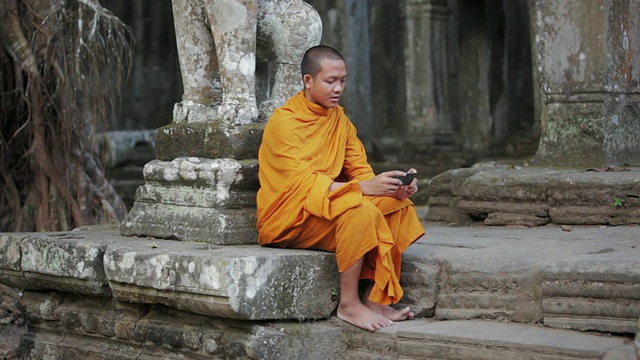 在柬埔寨暹粒吴哥窟(Angkor Wat / Siem Reap)一座古庙的台阶上，一名和尚在轻触智能手机的屏幕视频素材