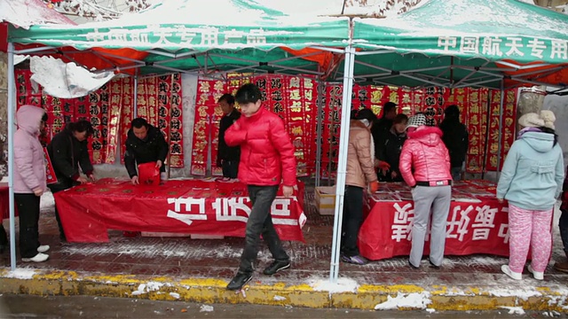 中国陕西西安，人们在雨雪天气的街道市场上购买春联视频素材