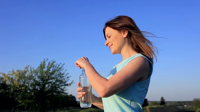 年轻女子喝着瓶子里的新鲜水。视频素材