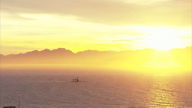 长镜头静止-当太阳升起时，海水流过一个灯塔。/南非视频素材