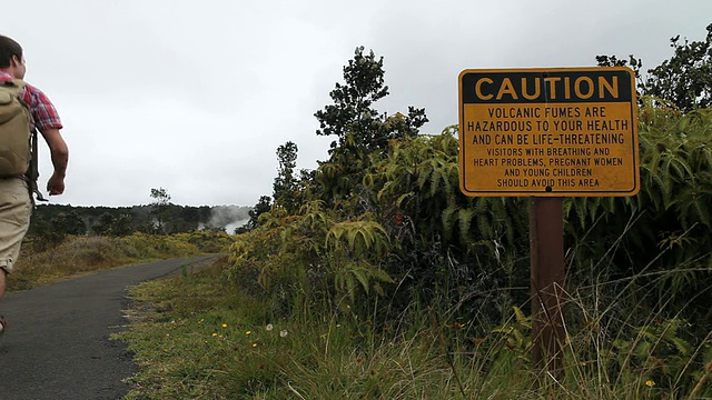 美国夏威夷火山国家公园/火山喷口的危险火山烟雾警告标志旁，一名穿着登山服的年轻男子离开视频素材