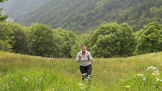 女人徒步穿越山地草地，鲜花视频素材