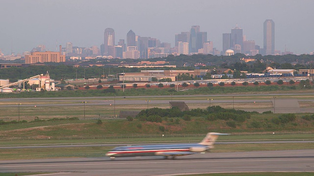 喷气式飞机(McDonnell Douglas MD-80)降落后穿过画面，背景是城市天际线/美国德克萨斯州达拉斯沃斯堡DFW国际机场视频素材