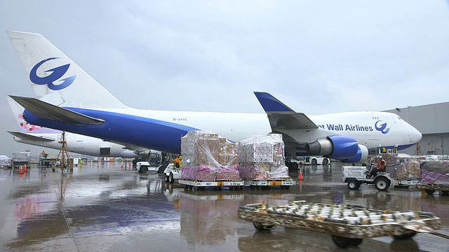 WS长城航空货运飞机(波音747-400F)在被雨打湿的停机坪上，前方是正在运送货物的卡车/美国德克萨斯州达拉斯沃斯堡国际机场视频素材