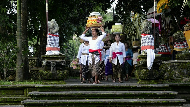 印度尼西亚巴厘岛乌布，从装饰多彩的Pura Dalem Puri寺庙中，妇女们头上顶着供品视频素材