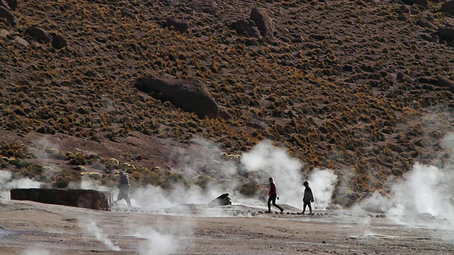 智利阿塔卡马沙漠，人们走过间歇泉田和从地面/ Geiser del Tatio冒出的蒸汽视频素材