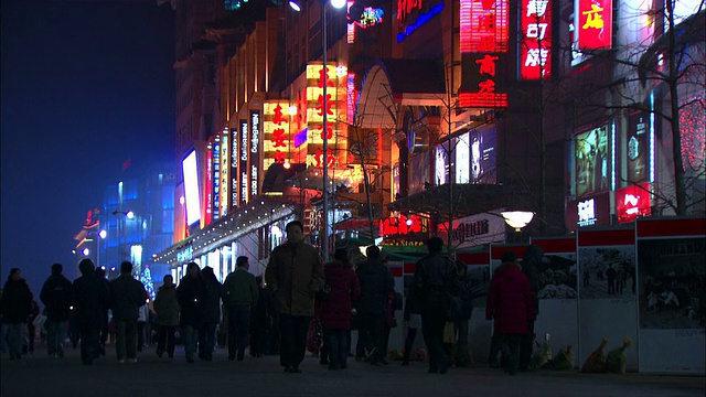 中远镜头倾斜——在北京一条挤满行人的街道上，霓虹灯闪烁。中国/北京视频素材