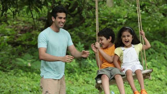 印度马哈拉施特拉邦，Malshej Ghat，一名男子在公园里摇晃他的孩子视频素材