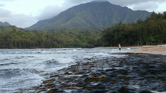 一名男子站在美国夏威夷考艾岛海滩的岩石海岸线上视频素材