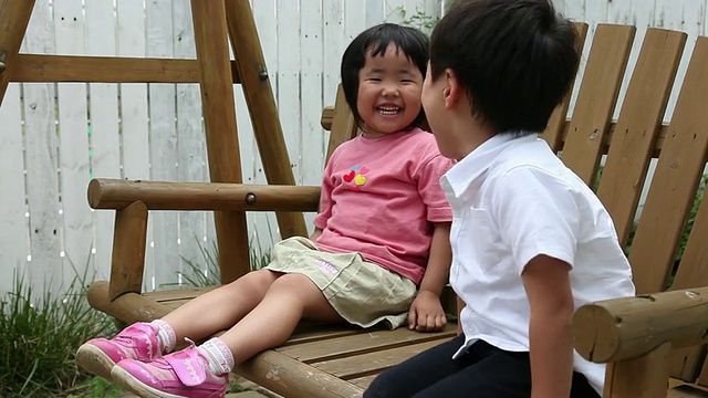 小男孩和小女孩在院子里的秋千上快乐地笑着视频素材