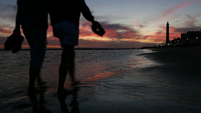 一对情侣在夕阳下漫步海滩。视频素材