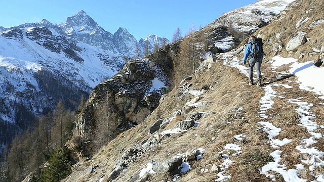 潘作为一个徒步旅行者沿着雪道，在草坡，山视频素材