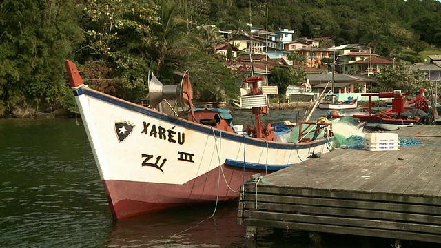 巴西Florianopolis [FlorianÃ³polis]郊区b/g的小渔船停靠在码头上，有水边住宅。[巴西]视频素材