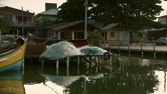 在巴西Florianopolis [FlorianÃ³polis]郊区，沿着水道移动，码头上堆积的渔网，水边住宅和船只[巴西]视频素材