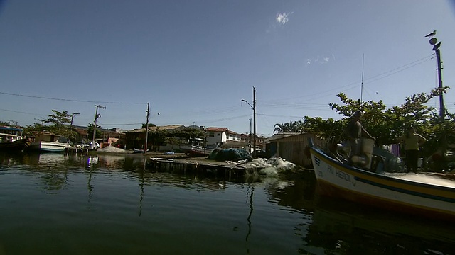 巴西Florianopolis [FlorianÃ³polis]郊区，沿着非常静止的水道移动，路过渔船和河边住宅的人们。视频素材