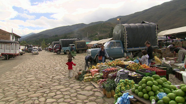 哥伦比亚，Villa De Leyva, BoyacÃ’department, Villa De Leyva市场边上的水果摊，孩子们和经过的汽车视频素材