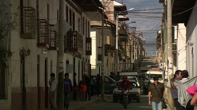 “在秘鲁Chachapoyas, De La Armas广场，你可以看到繁忙的小街，来来通常的人们，奔跑的人们，汽车在停着的汽车间穿梭，阳台和电力/电话/洗涤线电缆在上面纵横交错。[PerÃº]”视频素材