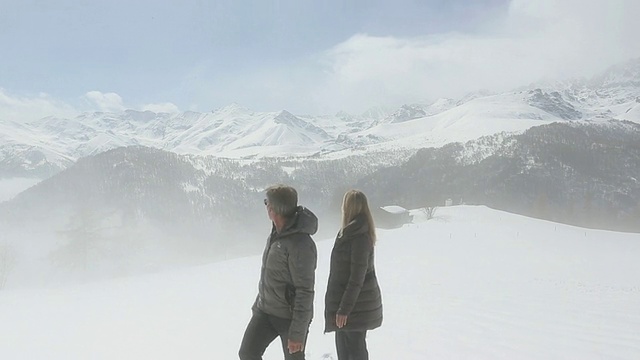 一对夫妇从雾气蒙蒙的山地草地上穿过雪地视频素材