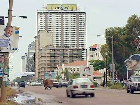 拍摄城市潮湿的街道，高楼大厦，开走的汽车和两名男子过马路/莫桑比克马普托视频素材