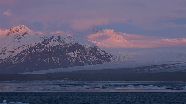 在冰岛的Jokulsarlon湖，日出的辉光照亮了Breidamerkurjokull冰川和雪山上的云视频素材