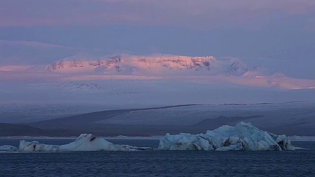 日出的辉光照亮了布莱德默库尔冰盖和冰川融化的Jokulsarlon湖上的雪山上的云/冰岛视频素材