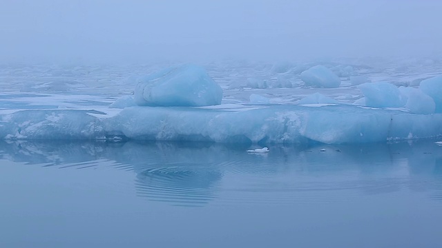 巨大的冰川在平静的Jokulsarlon礁湖表面上漂浮和漂流，涟漪在前面蔓延，冰川反映在水面/冰岛视频素材