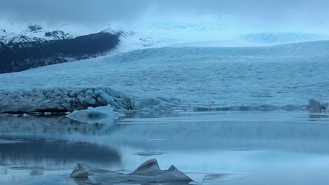 清晨，Fjallsarlon冰川反射并漂浮在湖面上，云朵在雪山/冰岛上空移动视频素材