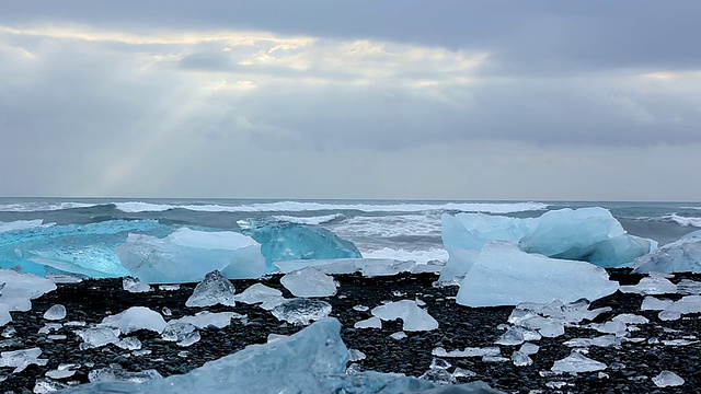 清晨在Jokulsarlon河口的Jokulsa冰山海滩上被冲刷的冰川，阳光通过云层/冰岛进入海洋视频素材