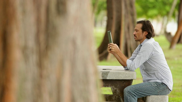 成熟的男人坐在桌子前使用平板设备，同时受到自然的启发视频素材