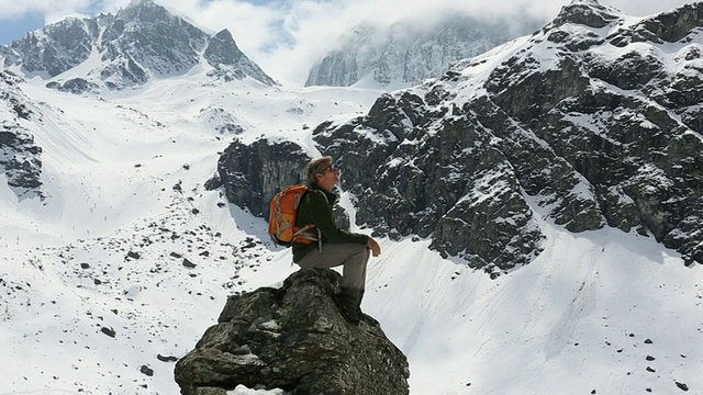 一个徒步旅行者坐在山顶上，看着雪山视频素材