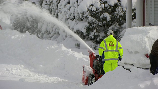 穿着黄色安全服的男子在人行道和街道上吹雪视频素材