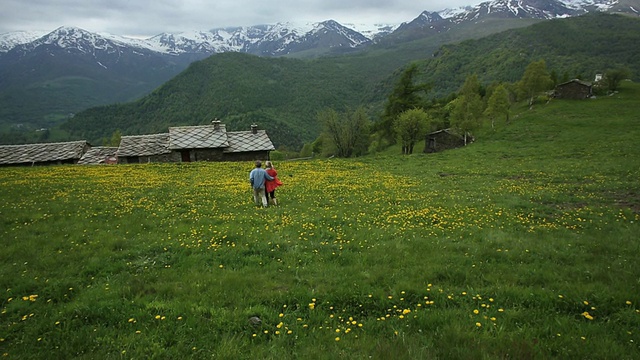 一对夫妇穿过山草地走向村庄视频素材