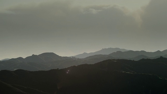 镜头摇摄马里布山，浓烟从远处的灌木丛大火从远处的山峰后面滚滚而起，太阳耀斑镜头视频素材