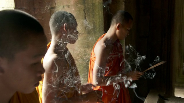 柬埔寨暹粒省吴哥城的巴戎寺，三名身穿橙色长袍的僧侣正在点香视频素材