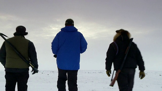 拍摄于加拿大努勒维特的Arviat，三个穿着雪服的男人在阳光和云的冰冻土地上行走视频素材