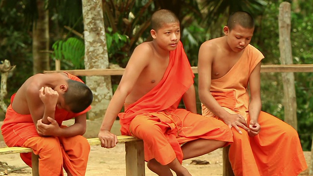 老挝琅勃拉邦Muang Ngoi附近的山村，三个小和尚坐在长凳上，其中一个正在检查肌肉视频素材