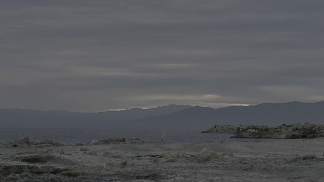 落日的余晖透过远处山脉上布满云的天空，透过原始景观和波澜起伏的索尔顿海，可以看到。视频素材