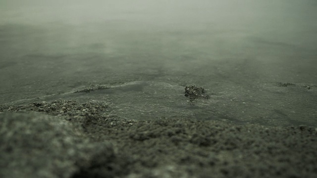 水轻轻地拍打着嶙峋的海岸，倒影着云雾覆盖的天空。视频素材