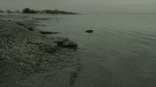 水轻轻地拍打着嶙峋的海岸，倒影着云雾覆盖的天空。视频素材