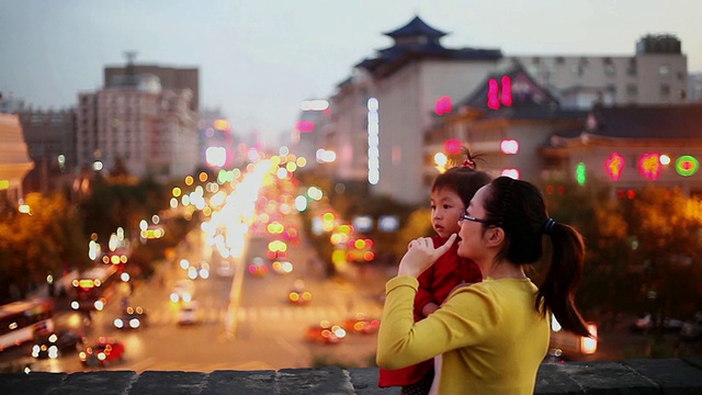 日落时分，母女俩在西安城墙上与城市交通交谈的照片/中国西安视频素材