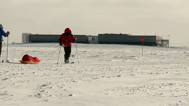 在南极项目基地/南极点，两个人在滑雪上拉着背包雪橇穿越南极冰视频素材