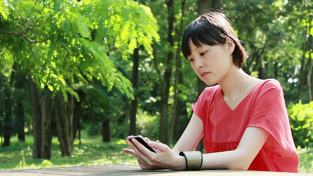 这是一名年轻女子在日本东京中野公园使用智能手机的照片视频素材