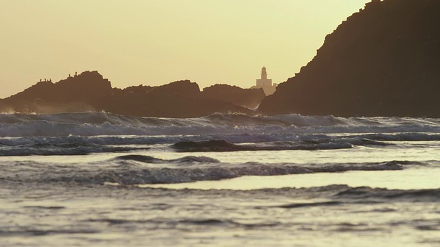 WS SLO MO灯塔的剪影映衬在多岩石的太平洋海岸，海浪拍打，日落时分，海鸥飞过/阿斯托里亚，俄勒冈，美国视频素材