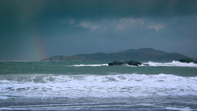 搅动的海浪打破海滩和岩石与彩虹和云/德拉姆贝格，苏格兰，英国视频素材